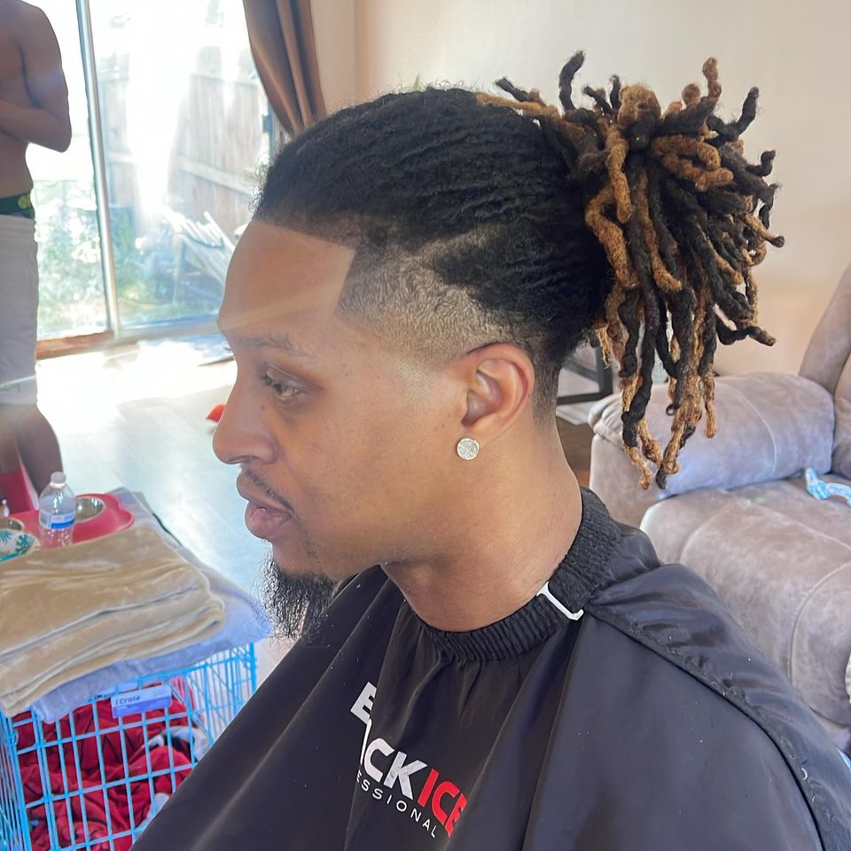 Side profile of a temple taper with a sharp shaved part and two-tone locs pulled up into a ponytail